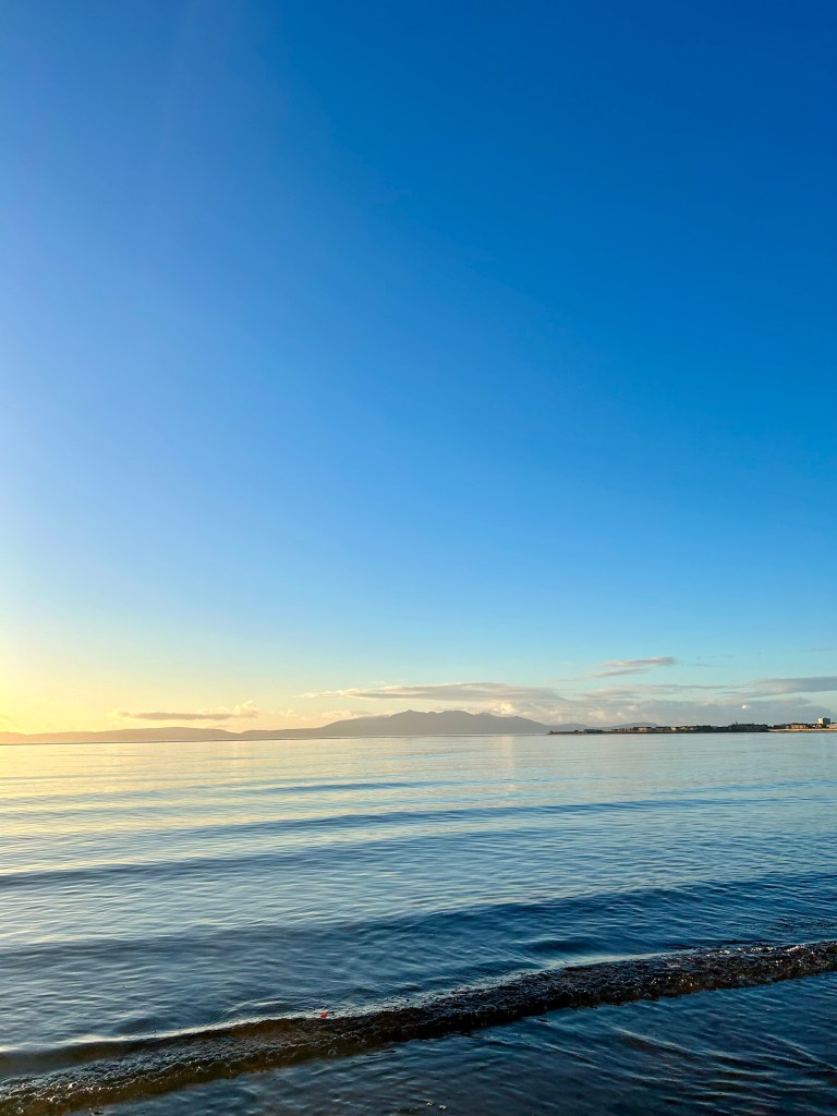 A glassy calm sea under a bright blue sky with distant island mountains.