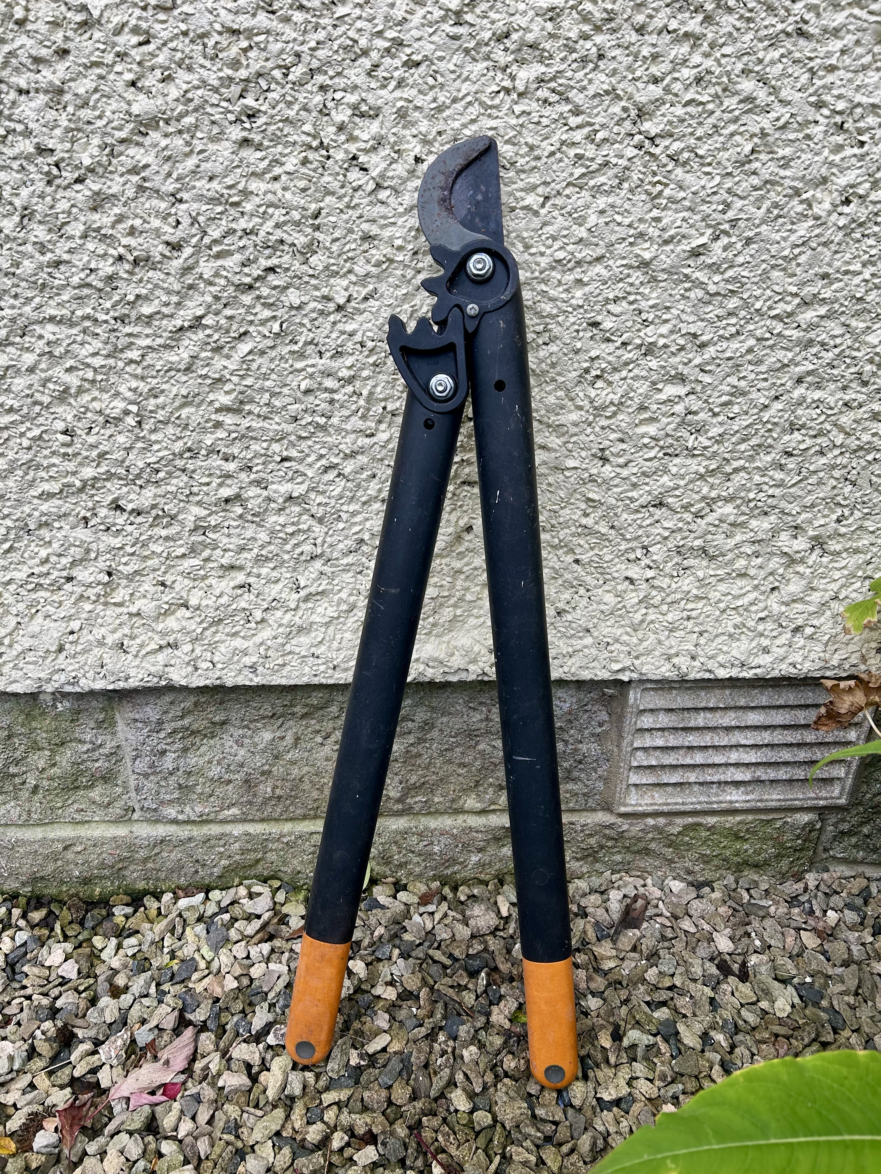 Orange handled loppers leaning against a cream wall.