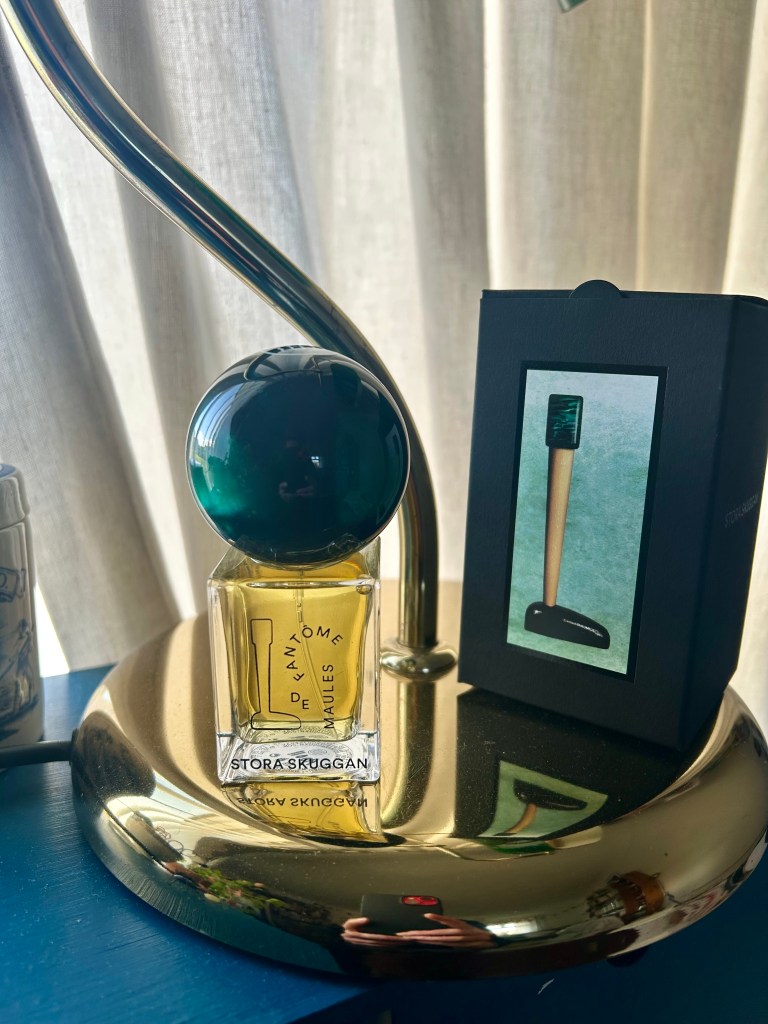 A bottle of  Fantome de Maules by Stora Skuggan has a swirled dark green spherical cap. It's next to its box on a brass lamp base.