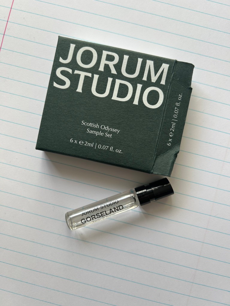 A small glass vial of Gorseland perfume by Jorum Studio is on a piece of lined white paper. There is a dark green box with Jorum Studio branding next to it.