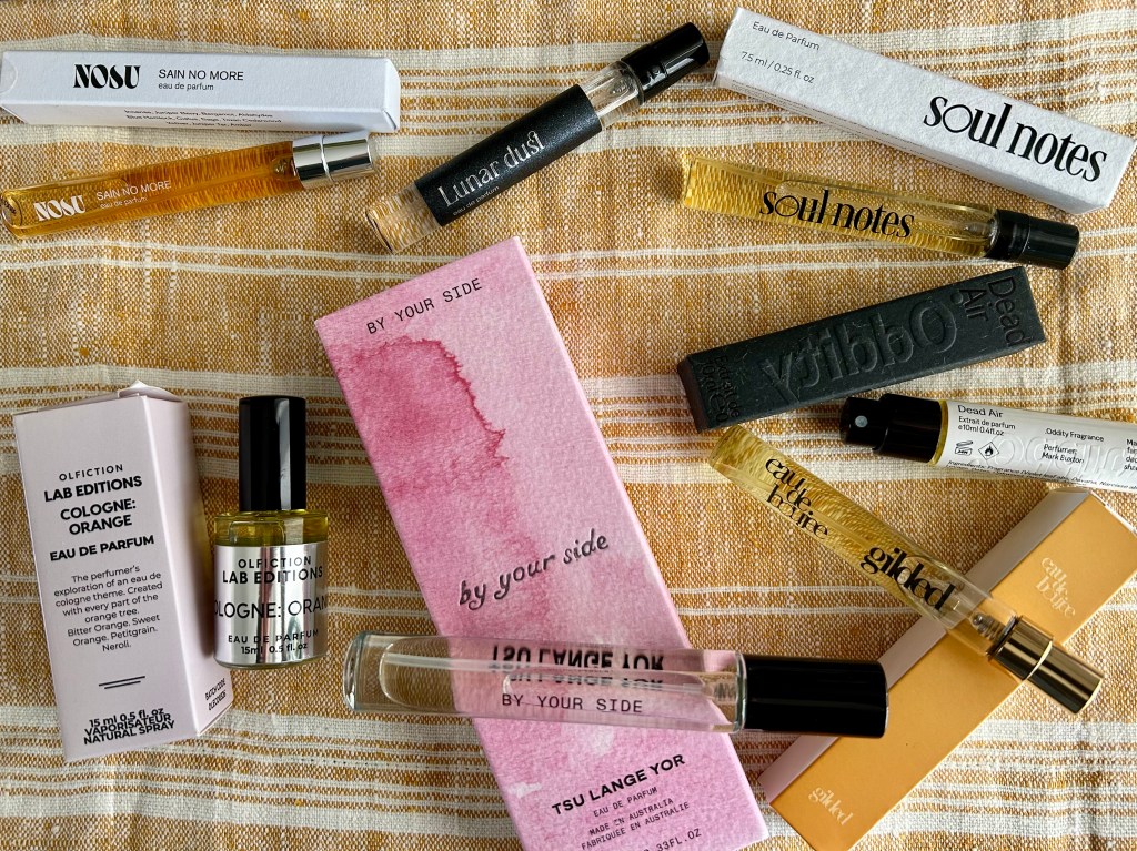 A selection of small glass bottles of indie perfume are resting on a yellow and white linen cloth.