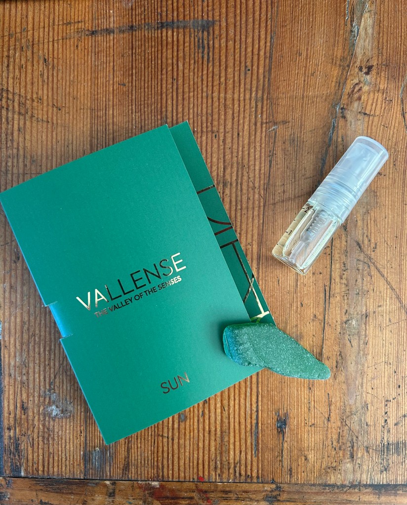 A small bottle of perfume is next to its green packaging and a piece of sea glass. Everything is on an antique pine chest.